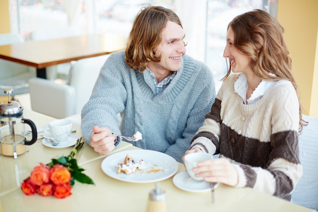 Portrait of amorous young couple talking by the dessert in restaurant or cafe