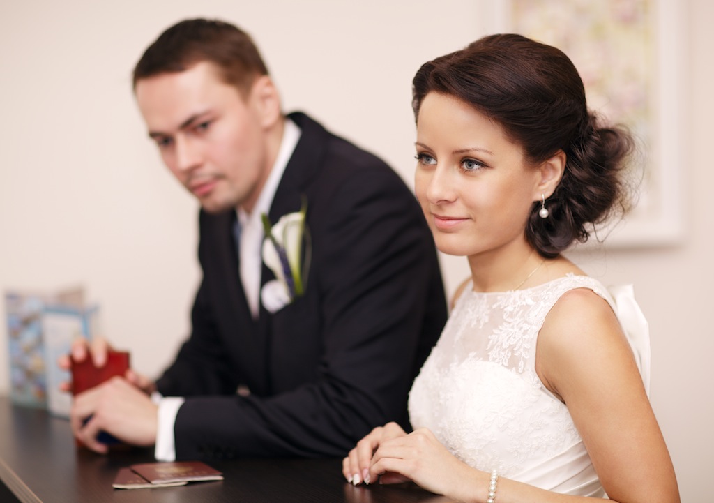Elegant young couple standing at a reception desk with their passports with the beautiful woman smiling as she waits for service