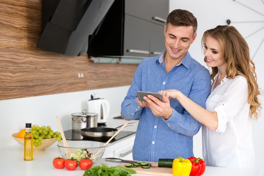 Beautiful couple using smartphone and cooking on the kitchen at home