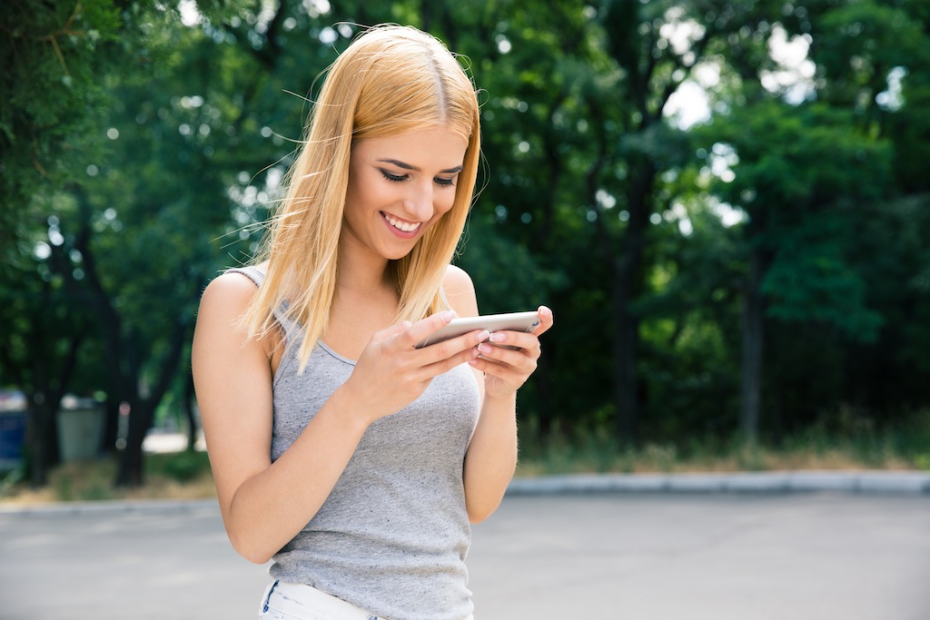 Happy young girl using smartphone outdoors