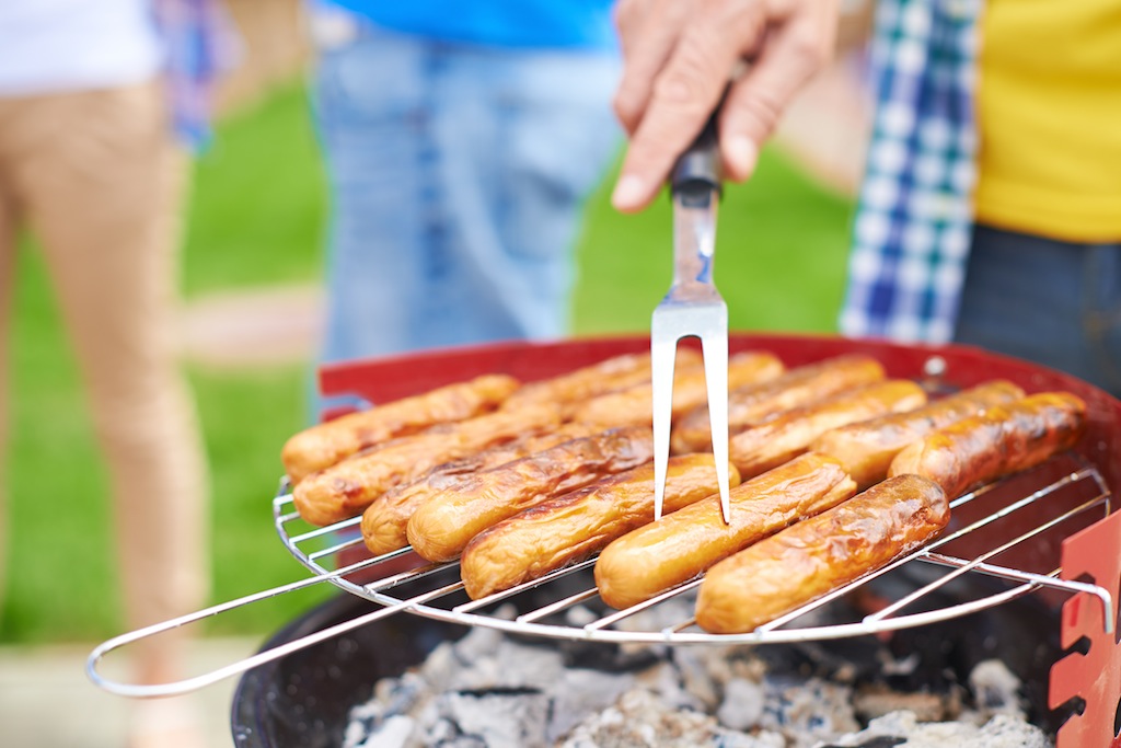 Human hand with fork frying sausages on grill at weekend