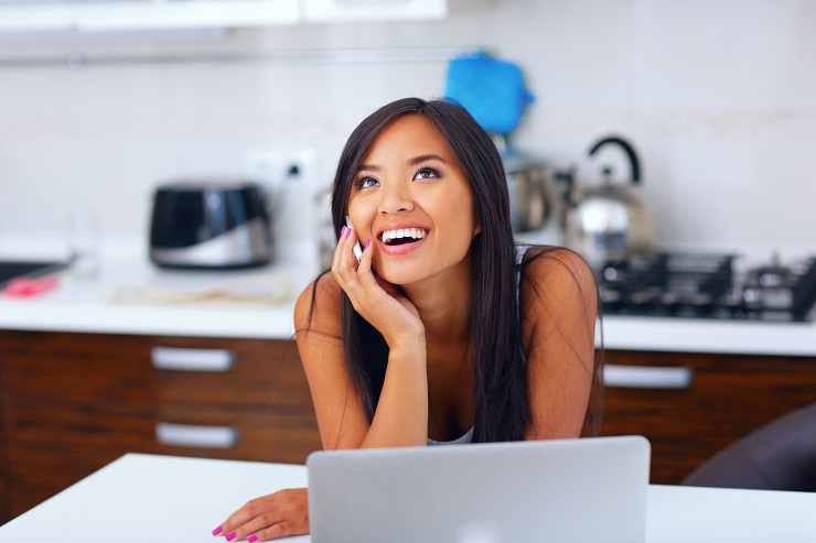 Laughing young asian woman talking on phone at home