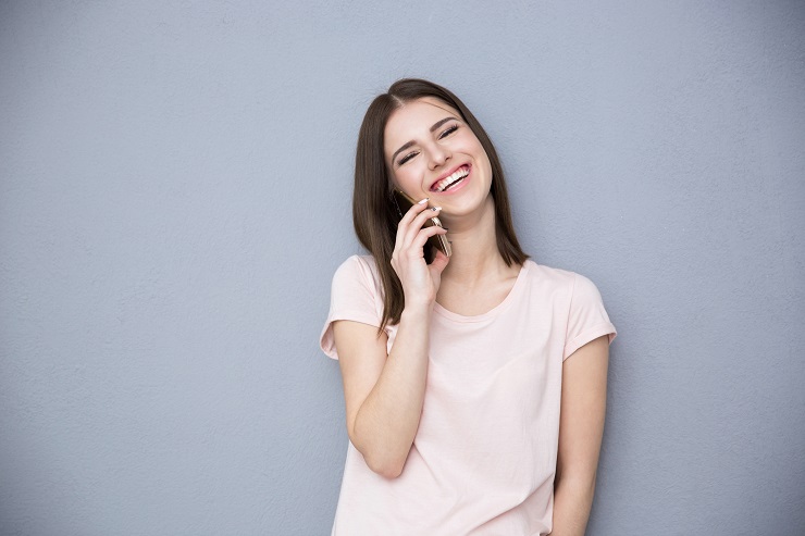Laughing young woman talking on the phone over gray background