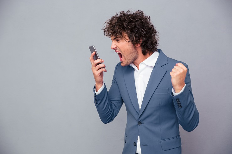 Portrait of angry businessman shouting on smartphone over gray background