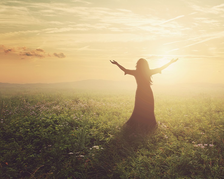 A woman lifts her arms in praise at dawn