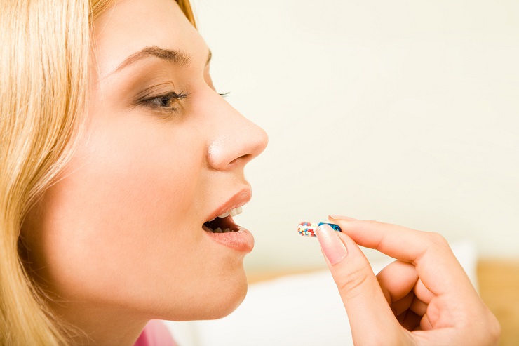 Profile of young woman holding pill by her mouth before taking it
