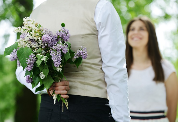 Portrait of a man hiding a flowers bouquet behind his back to surprise to a female